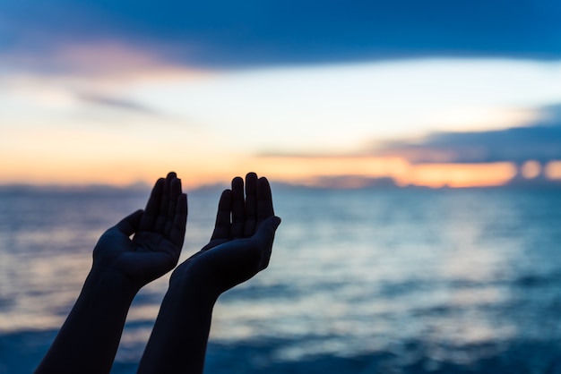 Foto siluetee las manos de la mujer que ruegan de dios durante puesta del sol, concepto de la esperanza.