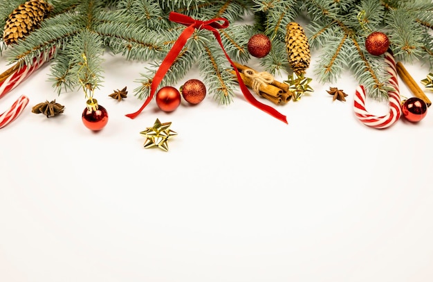 Silvester oder Weihnachten Urlaub Dekorationen Weihnachtsbaum Zweige rote Kugeln Kegel rote Bänder und Schleife Zimtstangen Anissterne und Lutscher auf weißem Hintergrund Platz für Text