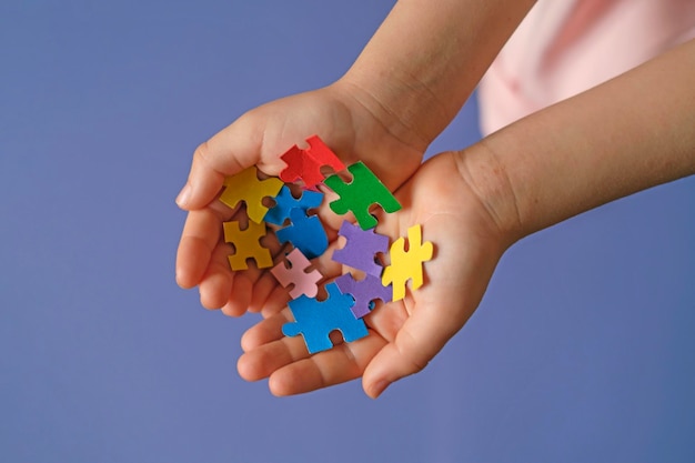 Un símbolo del autismo en forma de rompecabezas multicolores en las palmas de las manos de los niños