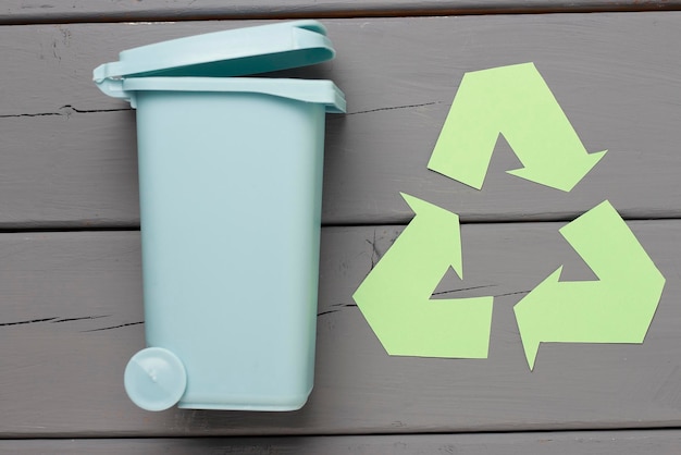 Un símbolo de basura de reciclaje verde y un bote de basura en una vista superior de fondo gris