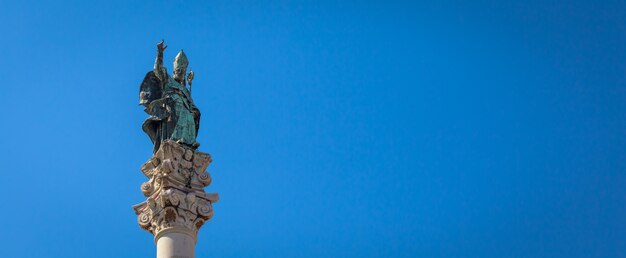 El símbolo de la ciudad de Lecce (Italia): San Oronzo (Sant'Oronzo) posado en la columna en el centro de la plaza principal de la ciudad. Fondo azul con espacio de copia.