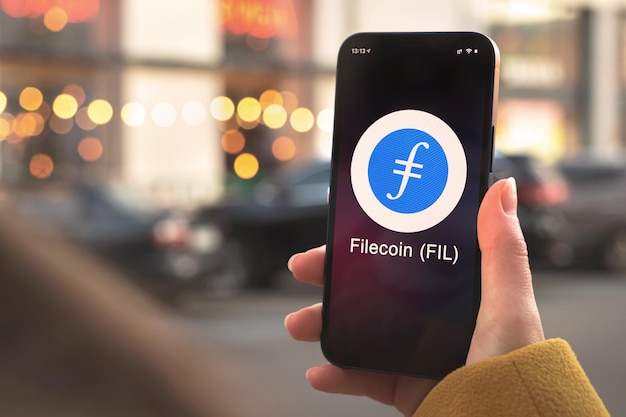 Símbolo de criptomoneda Filecoin FIL, logotipo. Concepto financiero y empresarial. Mano con smartphone, pantalla con primer plano del icono de criptografía