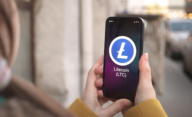 Símbolo de criptomoneda Litecoin LTC, logotipo. Concepto financiero y empresarial. Mano con smartphone, pantalla con primer plano del icono de criptografía