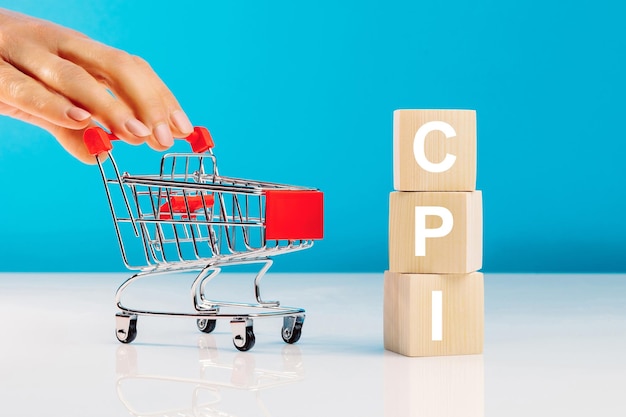 Símbolo do Índice de Preços ao Consumidor CPIBloco de letras na palavra CPI abreviatura do índice de preços ao consumidor e a mão da mulher empurrando o carrinho de compras vazio no fundo azul