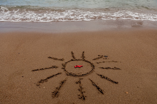 Símbolo do sol e um avião à beira-mar pintado de sol na areia do mar costa figura de um avião vermelho ondas do mar