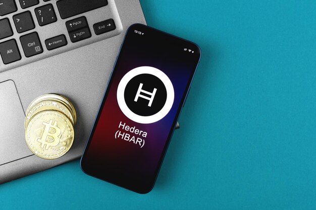 Símbolo de Hedera HBAR. Comercio con criptomonedas, dinero digital y virtual, banca con concepto de teléfono móvil. Espacio de trabajo empresarial, foto de vista superior de la mesa