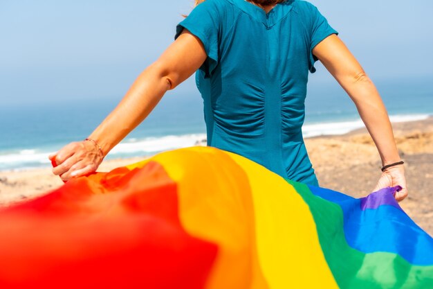 Símbolo lgbt, una lesbiana irreconocible desde atrás ondeando la bandera junto al mar