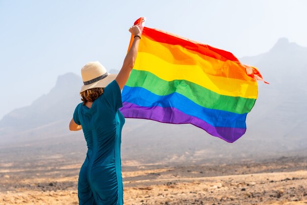 Símbolo lgbt, una persona lesbiana con un vestido verde y un sombrero blanco con la bandera del arco iris en el desierto