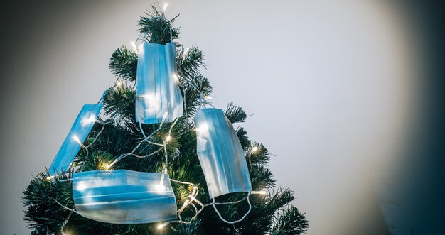 Símbolo del nuevo año que viene 2021. Máscaras médicas colgadas en el árbol de Navidad a la luz de guirnaldas. Días festivos durante la cuarentena por covid 19.