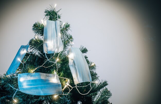 Símbolo del nuevo año que viene 2021. Máscaras médicas colgadas en el árbol de Navidad a la luz de guirnaldas. Días festivos durante la cuarentena por covid 19.