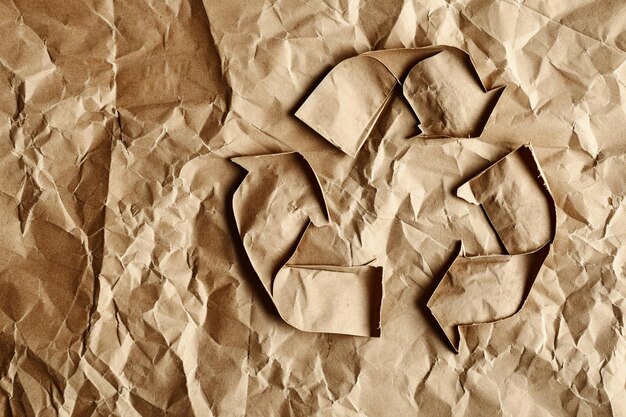 Foto símbolo de reciclaje de papel arrugado sobre fondo marrón