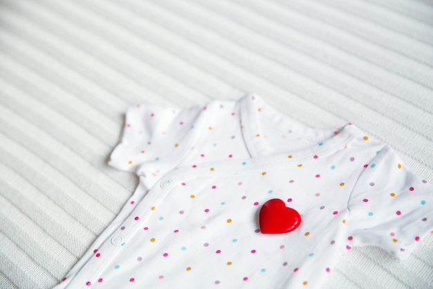 Símbolo de ropa de bebé de corazón sobre fondo de tela blanca.