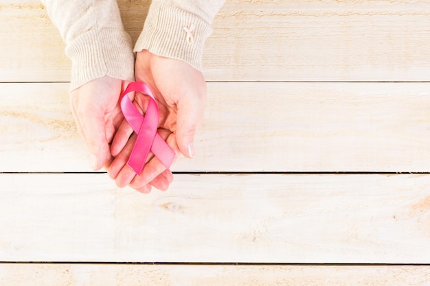 Símbolo de salud de la mujer en cinta rosa sobre tabla de madera.