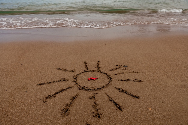 Símbolo del sol y un avión junto al mar sol pintado en la arena costa del mar figura de un avión rojo mar ...