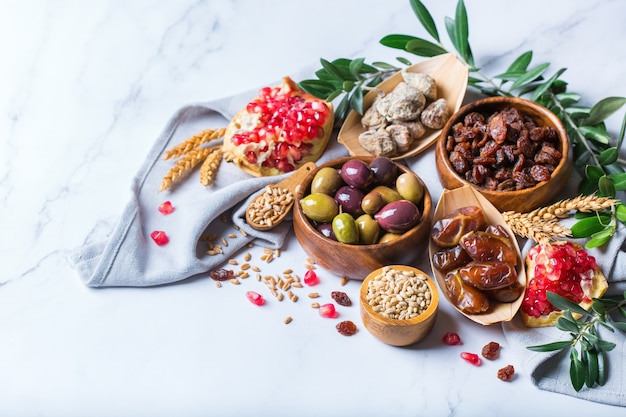 Símbolos do feriado judaico Tu Bishvat, Rosh Hashana, ano novo das árvores. Mistura de frutas secas, tâmara, figo, uva, cevada, trigo, azeitona, romã em uma mesa de mármore. Copie o fundo do espaço