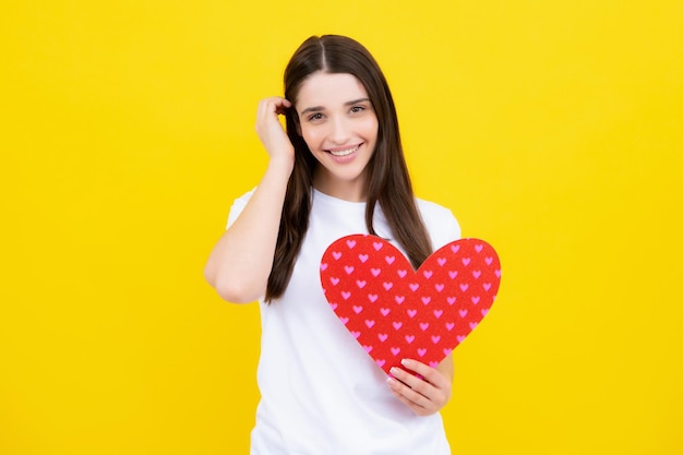 Símbolos de signos de amor para el feliz día de San Valentín o cumpleaños de las mujeres Encantadora chica encantadora sosteniendo en las manos el símbolo de amor del corazón aislado sobre fondo amarillo