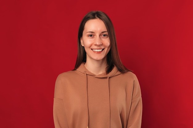 Simple retrato de estudio de una joven mujer sonriente sobre fondo rojo.