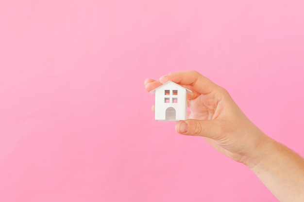 Simplemente diseñe la mano femenina femenina que sostiene la casa de juguete blanca miniatura aislada en fondo de moda colorido en colores pastel rosado