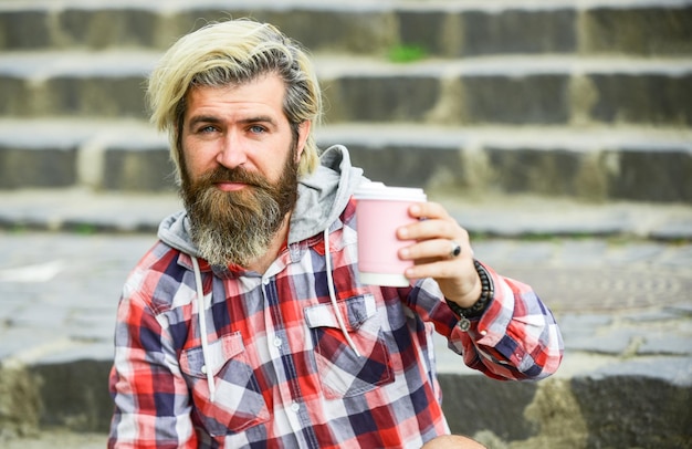 Simplemente relajante hombre brutal con barba bebiendo té de una taza hombre barbudo beber café hipster al aire libre relajarse en las escaleras viajero maduro descansando para llevar café buenos días inspiración