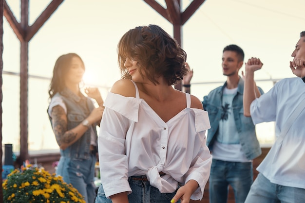 Simplemente relájese, una mujer joven y bonita con camisa blanca está sonriendo mientras está de pie en la azotea