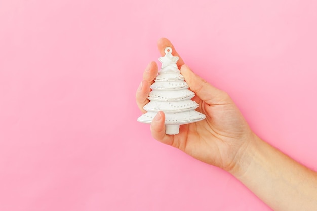 Simplesmente design mínimo feminino mão de mulher segurando enfeite de natal árvore de abeto isolada em rosa pastel.