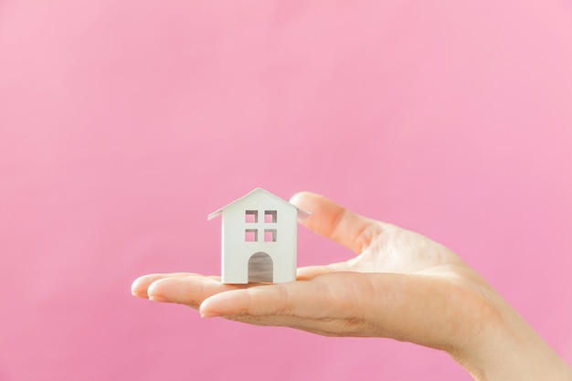 Simplesmente projete a mão de mulher feminina segurando a casa de brinquedo branco em miniatura isolada na moda colorida pastel rosa