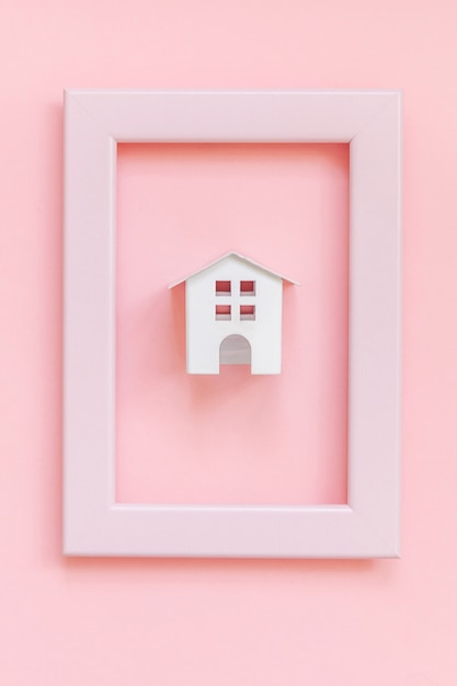 Simplesmente projete com casa de brinquedo branco em miniatura no quadro rosa isolado no fundo na moda colorido pastel rosa