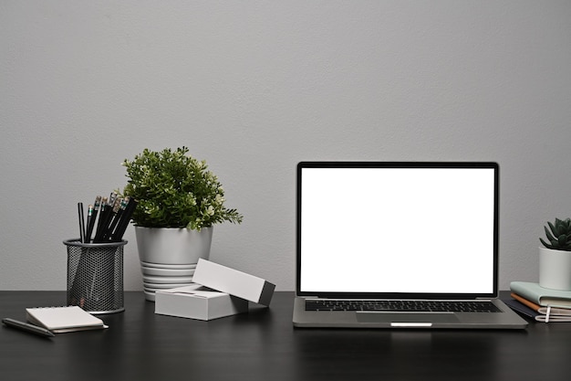 Simulacros de computadora portátil con pantalla en blanco sobre una mesa negra en la oficina en casa.