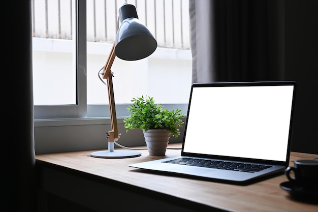 Simulacros de computadora portátil con planta en maceta de pantalla blanca y decoraciones de suministros en la mesa de madera