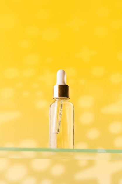 Simulacros de cuentagotas de vidrio con cosméticos para el cuidado antienvejecimiento en un estante de vidrio sobre un fondo amarillo Cuidado de la piel facial