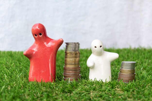 Simulacros de estatua familiar y pila de monedas en el piso de hierba con fondo blanco.