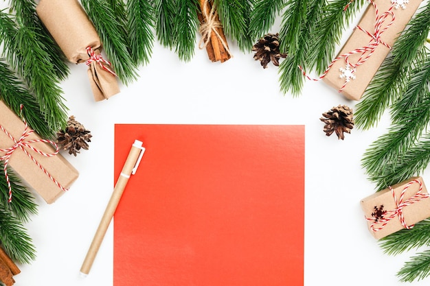 Simulacros de postales vacías rojas en la mesa blanca en el marco de las ramas de los árboles de navidad con conos y paquete ...