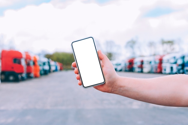 Simulacros de un smartphone en la mano de un hombre. En el contexto de los camiones rojos. Concepto de logística.