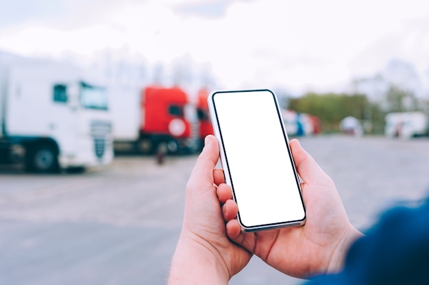 Foto simulacros de un smartphone en manos de un hombre. en el contexto de los camiones rojos. concepto de logística.