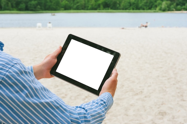 Simulacros de tableta en manos de un hombre. Con el telón de fondo de la playa y el río.