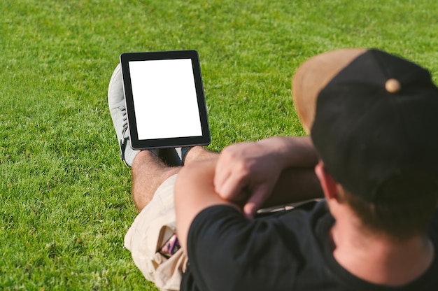 Simulacros de tableta a los pies de un chico de fitness. En el césped verde.