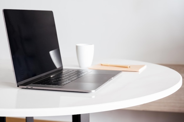 Simule una computadora portátil con pantalla en blanco y una taza de café con otros suministros de oficina