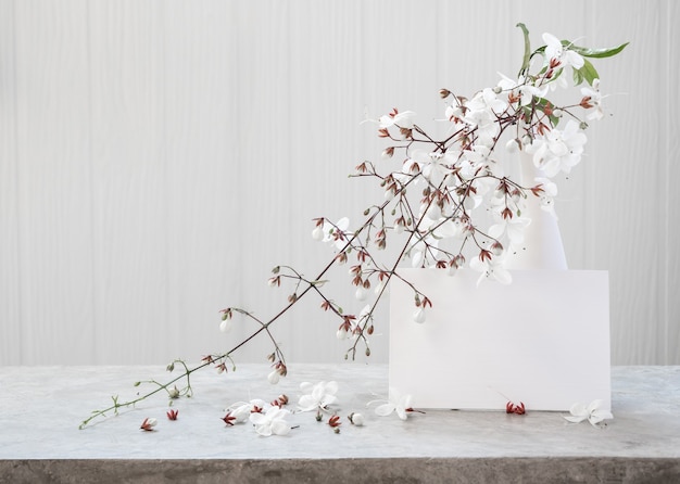 Foto simule um cartão de convite branco e lindas flores de clerodendro em um vaso moderno colocado na mesa de concreto