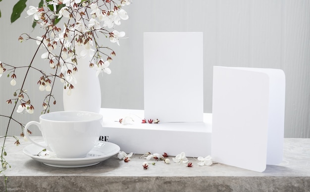 Foto simule um cartão de convite branco, um livro de xícaras de café e lindas flores de clerodendro em um vaso moderno colocado na mesa de concreto