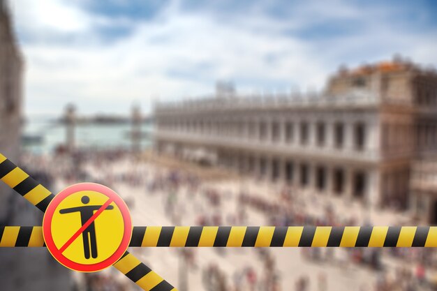 Sinal amarelo de aviso com homem riscado em um cruzamento de fitas de esgrima em um fundo desfocado do Palácio do Doge em Veneza, Itália. Coronavirus, pandemia de Covid 19, conceito de quarentena.