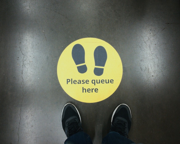 Sinal de alerta amarelo para manter a fila durante o surto de coronavírus covid-19 com passos na loja e pernas de duas pessoas no Reino Unido