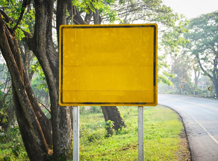 Foto sinal de informação amarelo junto ao tronco de uma árvore no parque