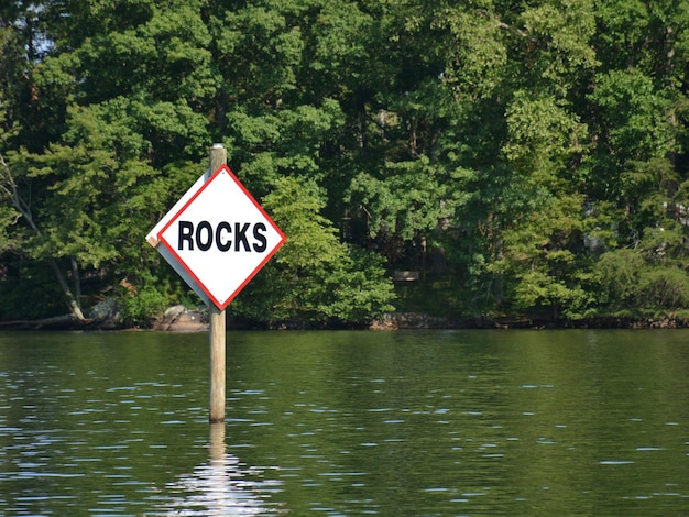 Foto sinal de informação por lago contra árvores advertindo de rochas