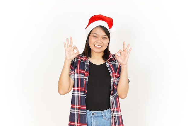Sinal de OK Gesto de linda mulher asiática vestindo camisa xadrez vermelha e chapéu de Papai Noel isolado no branco