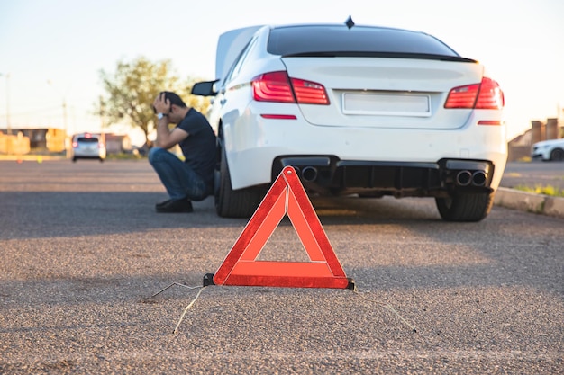 Sinal de parada de emergência e homem perto de carro quebrado