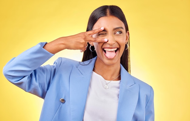 Sinal de paz engraçado e mulher com língua para fora e moda com gesto de mão emoji em estúdio fundo amarelo pessoa feminina sorriso e v com estilo moderno de liberdade e trabalhador com confiança feliz