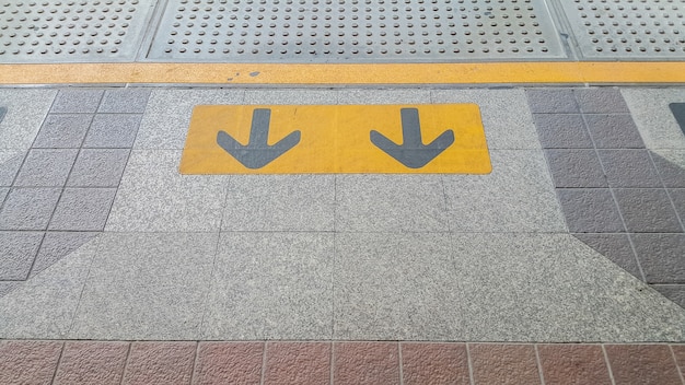 sinal de seta na cor amarela pintado em preto na zona de espera de trem, metrô