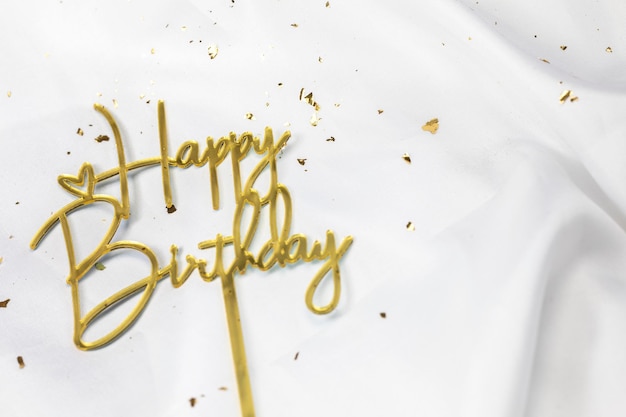 Sinal de texto de feliz aniversário bastão de topper em fundo de cetim branco conceito de celebração festiva de ouro cintilante