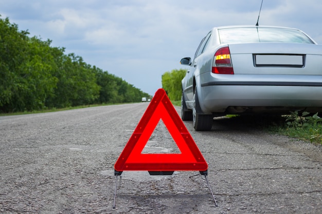 Sinal vermelho de parada de emergência e quebrado carro prateado na estrada