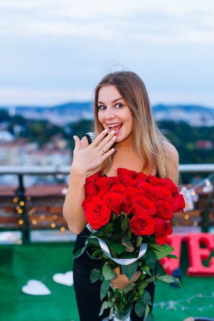 Sincera emoción de la niña en su dedo anular un anillo dorado y sostiene un ramo de flores